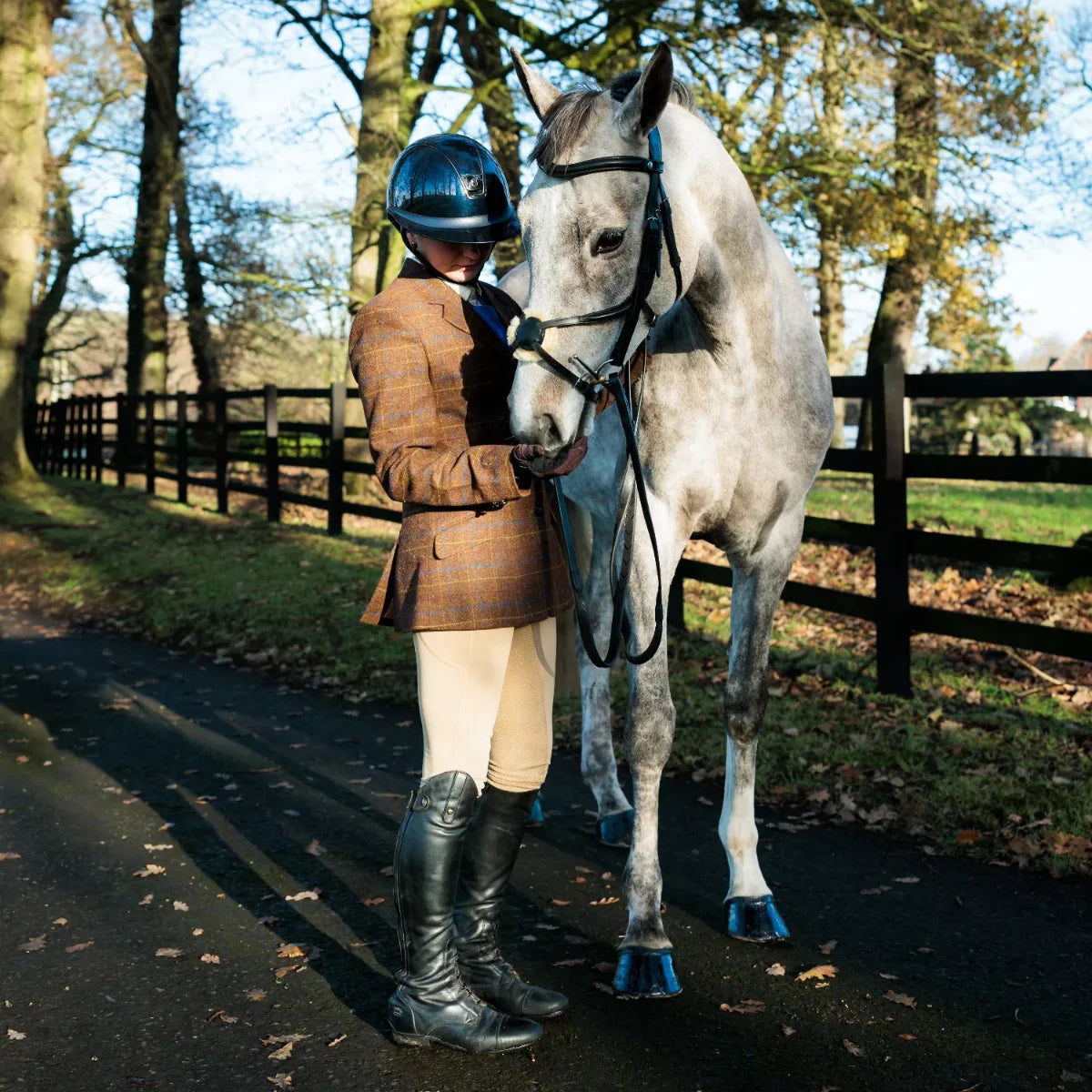 Dapple grey horse wearing an EcoRider grackle leather bridle, presented by an equestrian handler in a classic tweed jacket.