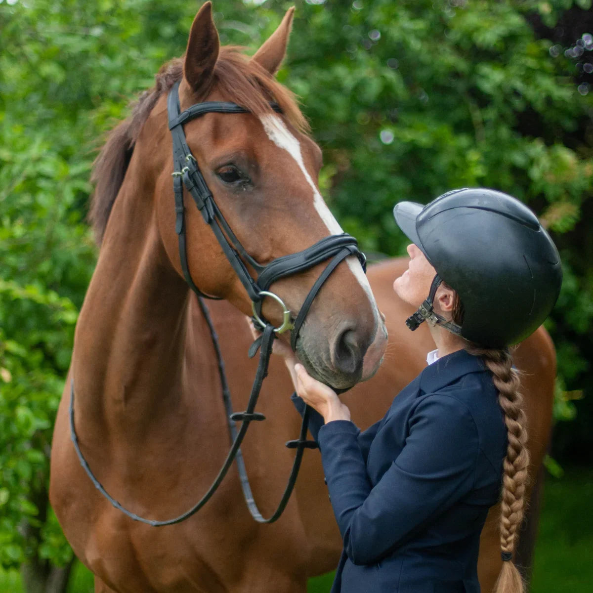 Equestrian handler standing with a chestnut horse wearing a black EcoRider anatomical bridle, showing a moment of connection.